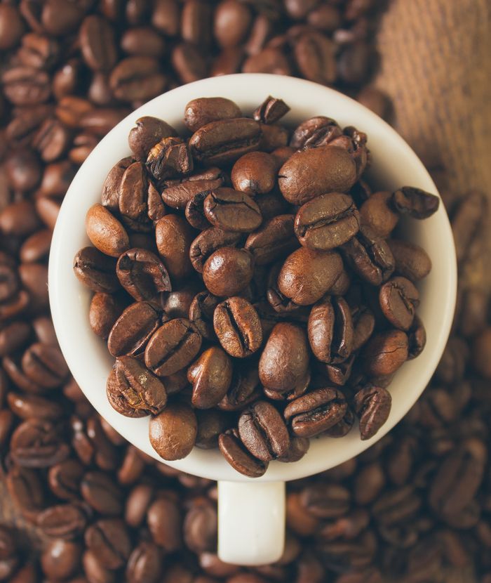 High-quality close-up image of roasted coffee beans in a cup on a wooden table.
