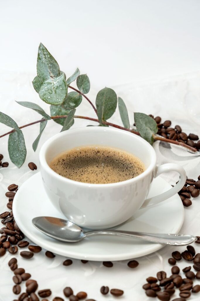 A steaming cup of coffee surrounded by beans and eucalyptus leaves, creating a serene morning ritual.